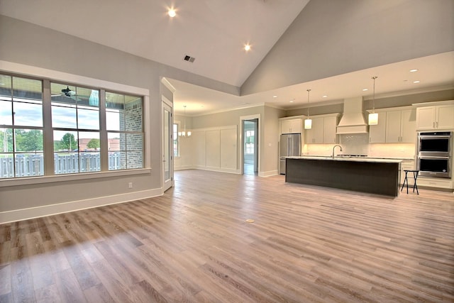 unfurnished living room with ornamental molding, high vaulted ceiling, a chandelier, and light hardwood / wood-style flooring