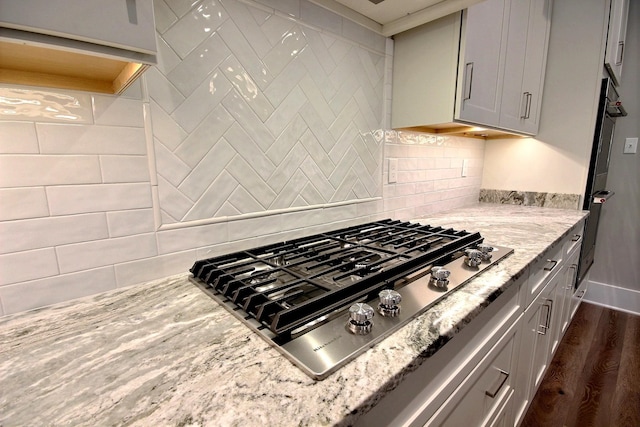 kitchen with light stone countertops, decorative backsplash, stainless steel gas stovetop, and dark hardwood / wood-style floors