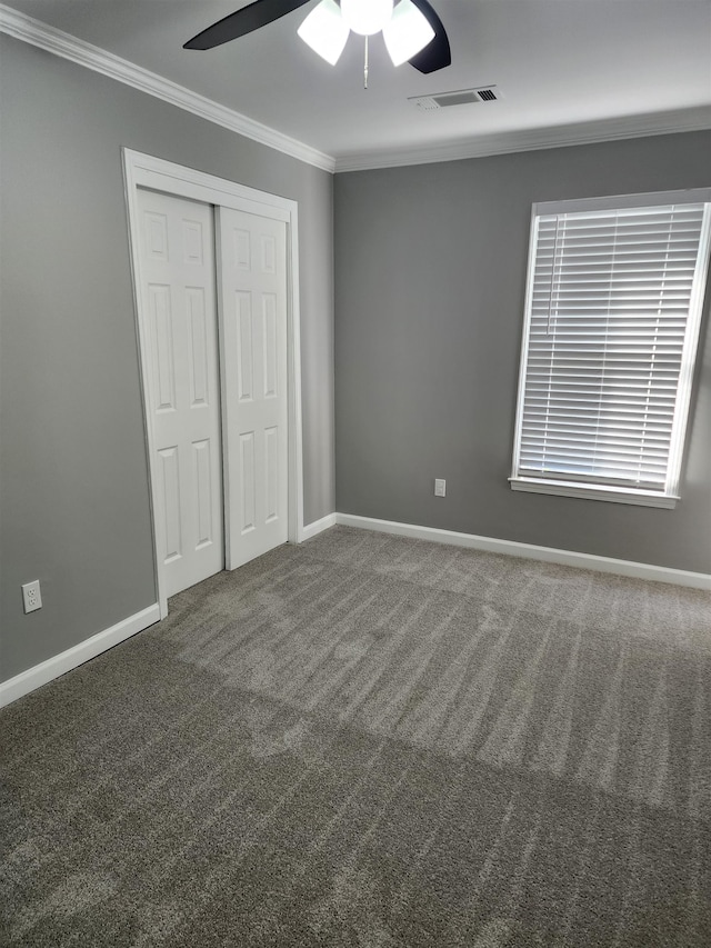 unfurnished bedroom featuring ceiling fan, a closet, crown molding, and dark carpet