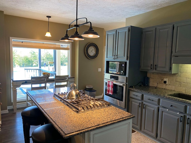 kitchen featuring stone counters, tasteful backsplash, a center island, stainless steel appliances, and dark wood-type flooring