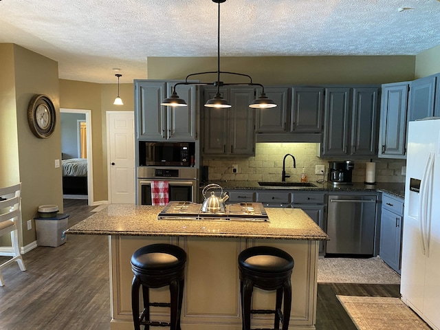 2845 Gilchrist Stantonville Rd, Stantonville, TN 38379 - kitchen featuring a textured ceiling, a sink, stainless steel appliances, a kitchen bar, and dark wood-type flooring