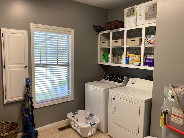 laundry area with electric water heater, a textured ceiling, washer and clothes dryer, and light tile patterned floors