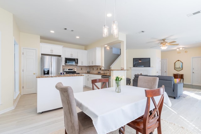 dining area featuring a fireplace, light hardwood / wood-style floors, sink, and ceiling fan