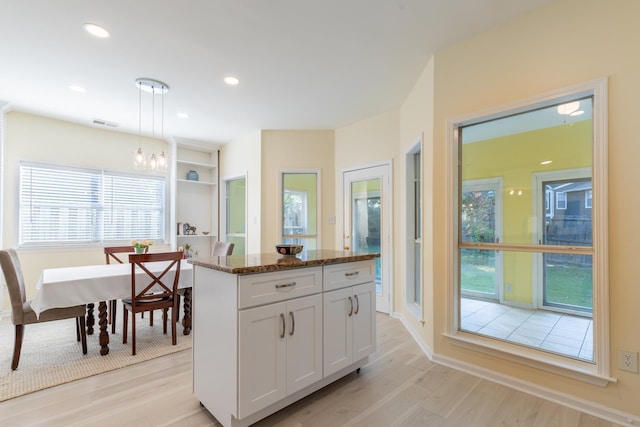 kitchen featuring hanging light fixtures, white cabinets, light hardwood / wood-style flooring, and dark stone countertops