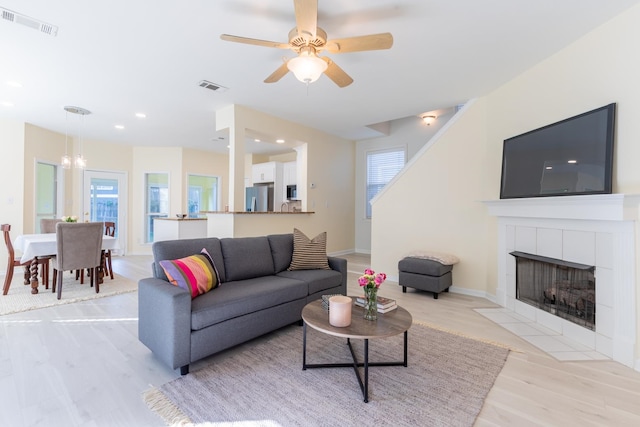 living room featuring ceiling fan with notable chandelier, a fireplace, and light hardwood / wood-style flooring