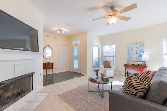 living room with ceiling fan, light wood-type flooring, and a tile fireplace