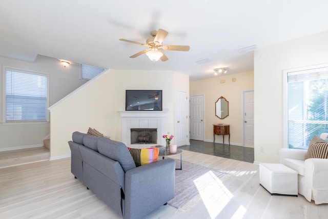 living room with ceiling fan, light hardwood / wood-style floors, and a tiled fireplace