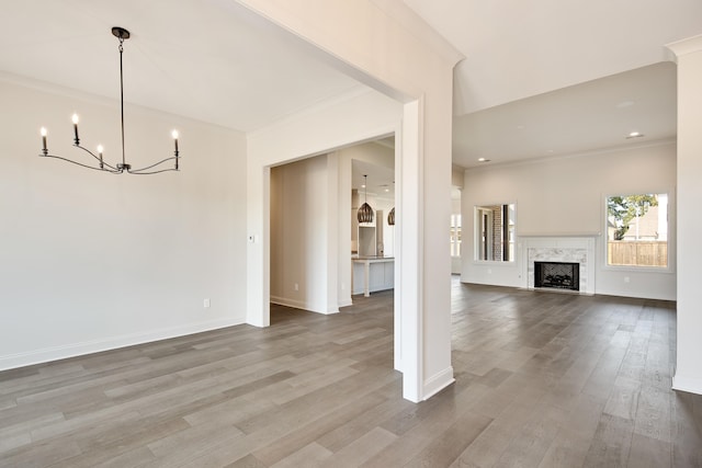 unfurnished living room featuring a premium fireplace, crown molding, hardwood / wood-style floors, and a chandelier