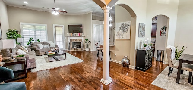 living room featuring ceiling fan, dark wood-type flooring, crown molding, a towering ceiling, and ornate columns