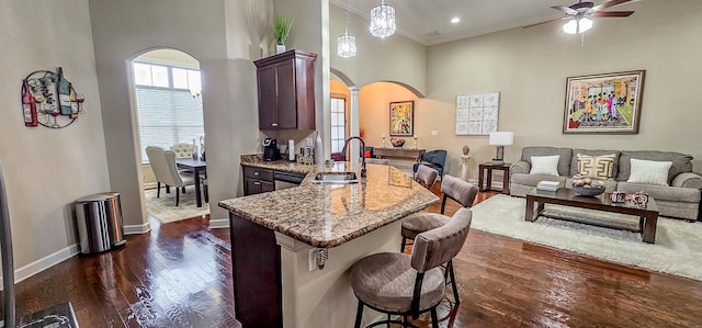 kitchen featuring ceiling fan, sink, dark wood-type flooring, a breakfast bar area, and a towering ceiling