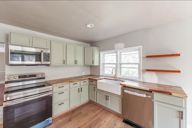 kitchen featuring light wood-type flooring, green cabinets, sink, butcher block countertops, and appliances with stainless steel finishes