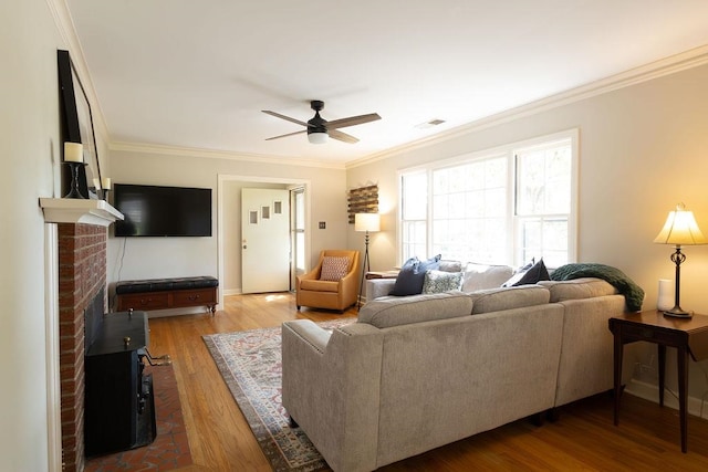 living room featuring ceiling fan, ornamental molding, a brick fireplace, and hardwood / wood-style floors