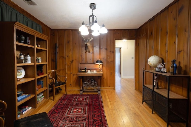 interior space with light hardwood / wood-style floors, wooden walls, a chandelier, and ornamental molding