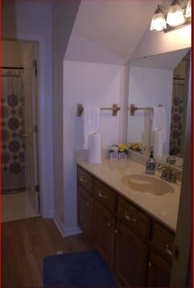 bathroom with wood-type flooring, vanity, vaulted ceiling, and curtained shower