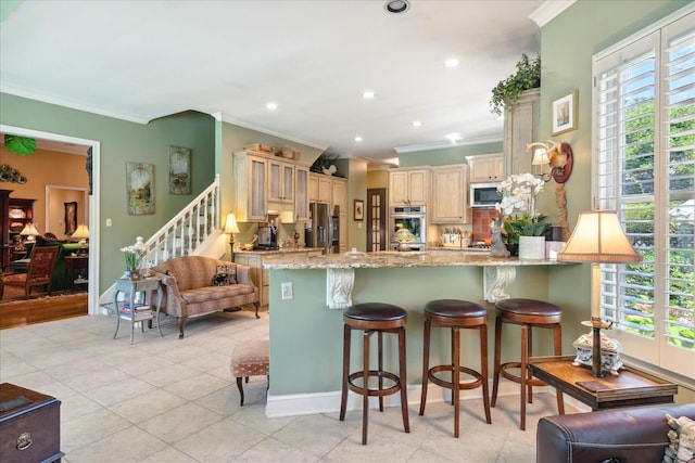 kitchen with light stone counters, stainless steel appliances, light tile patterned flooring, crown molding, and a kitchen bar