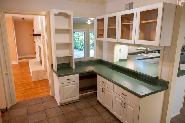 kitchen with white cabinets, sink, a brick fireplace, dark wood-type flooring, and crown molding