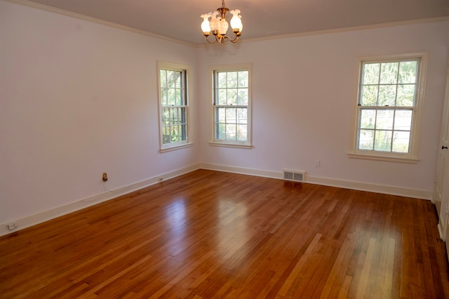 empty room featuring wood-type flooring, crown molding, and an inviting chandelier