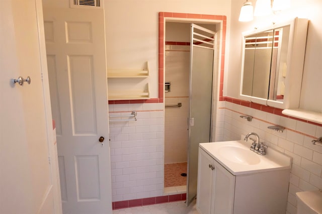 bathroom featuring vanity, tile walls, toilet, and tiled shower