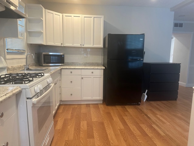 kitchen with light wood-type flooring, exhaust hood, white cabinets, black fridge, and white gas range oven