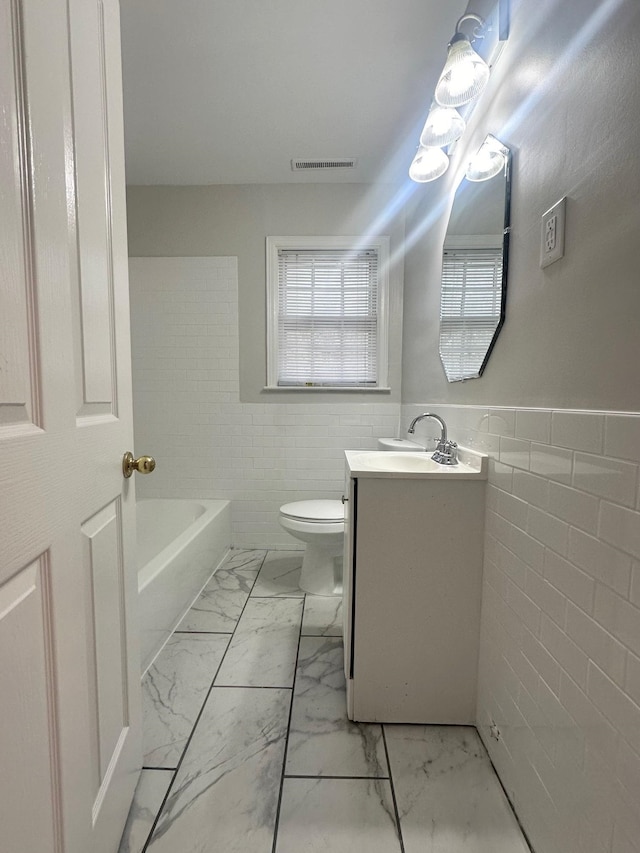 bathroom featuring a bathing tub, vanity, tile walls, and toilet