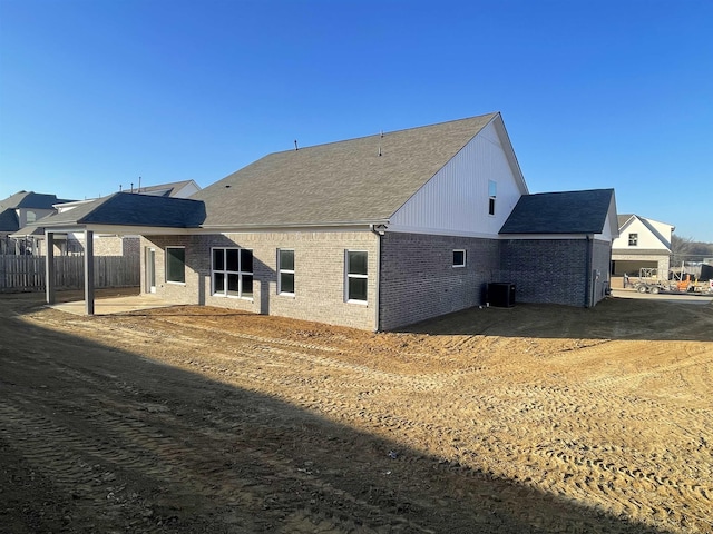 back of house featuring central AC, brick siding, a patio, and a shingled roof