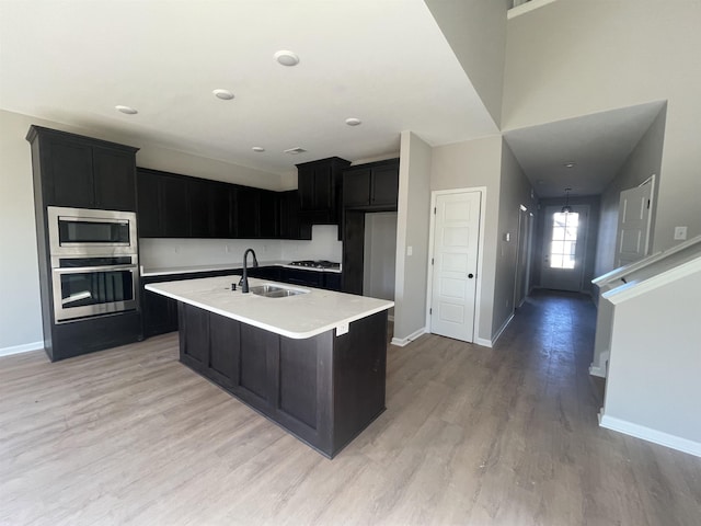 kitchen featuring appliances with stainless steel finishes, sink, an island with sink, and light hardwood / wood-style flooring