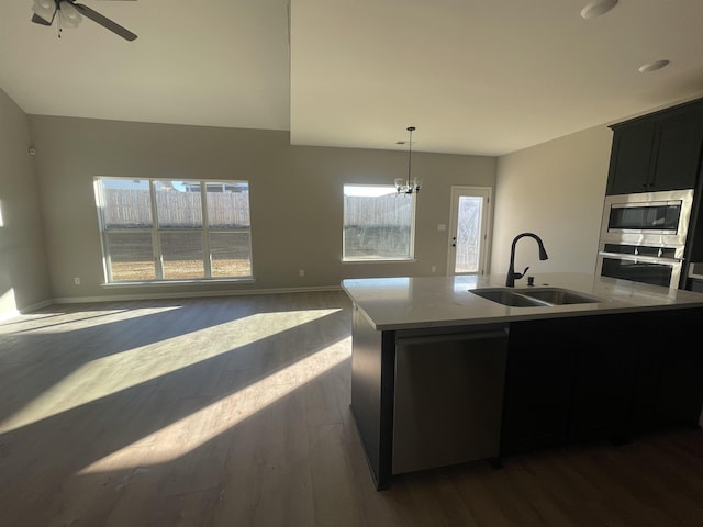 kitchen featuring open floor plan, a kitchen island with sink, stainless steel appliances, pendant lighting, and a sink