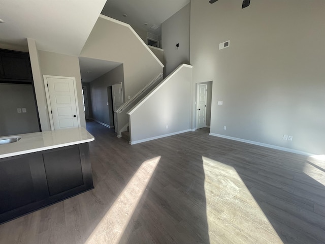 unfurnished living room featuring baseboards, visible vents, dark wood-type flooring, a high ceiling, and stairs