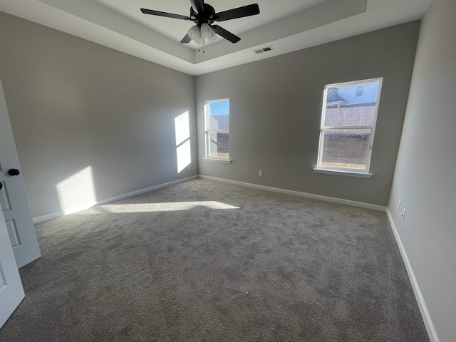 carpeted spare room featuring ceiling fan, a raised ceiling, visible vents, and baseboards