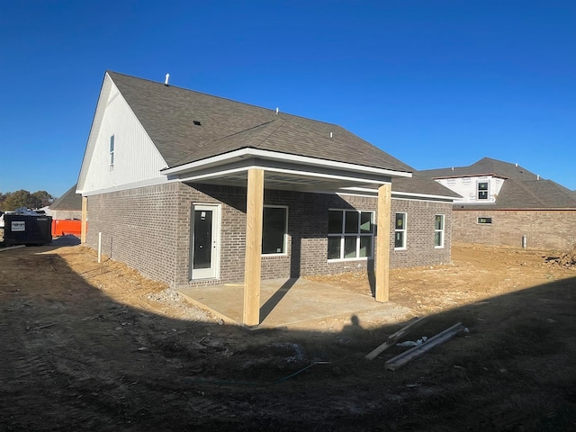 back of property featuring brick siding, roof with shingles, and a patio area