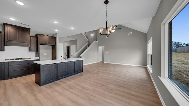 kitchen with an island with sink, open floor plan, light countertops, dark brown cabinets, and a sink