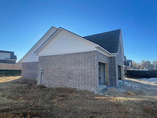 view of side of property featuring brick siding and roof with shingles