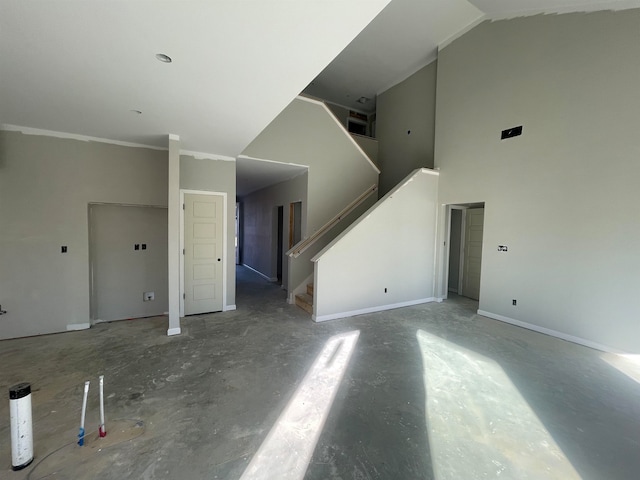 unfurnished living room featuring high vaulted ceiling, stairway, and baseboards