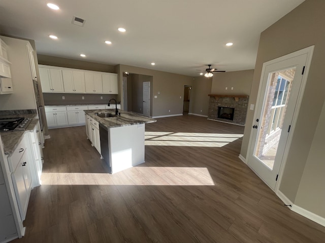 kitchen with sink, an island with sink, white cabinets, dark hardwood / wood-style flooring, and a stone fireplace