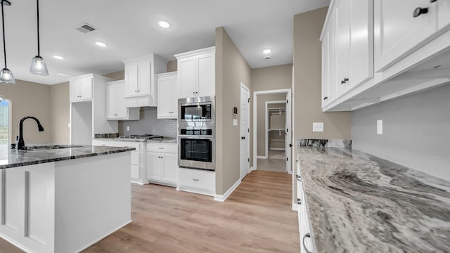 kitchen with pendant lighting, dark stone counters, white cabinets, and appliances with stainless steel finishes