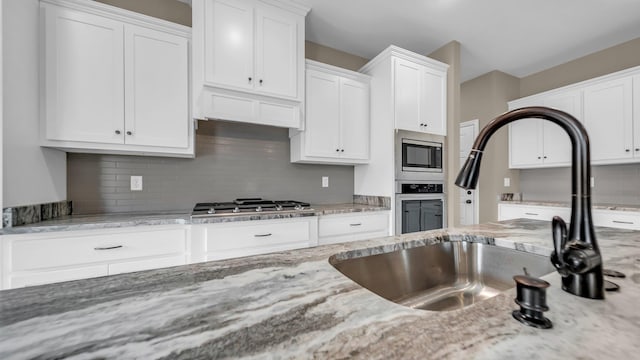 kitchen with light stone countertops, appliances with stainless steel finishes, white cabinets, and backsplash