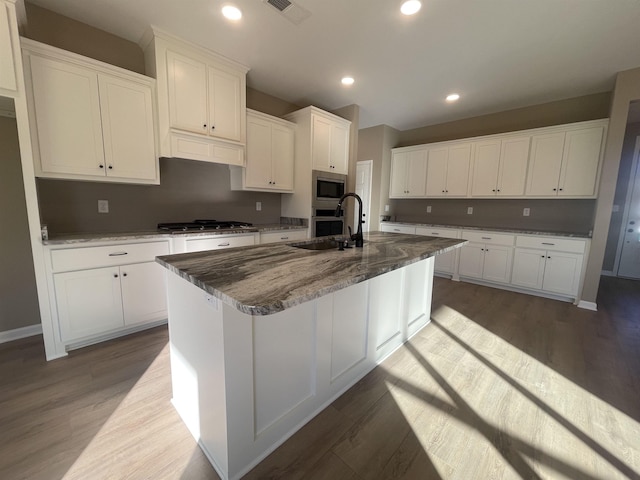 kitchen with white cabinetry, appliances with stainless steel finishes, a kitchen island with sink, and dark stone countertops