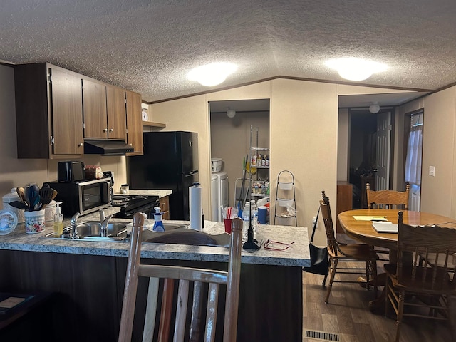 kitchen with a textured ceiling, black refrigerator, dark wood-type flooring, and vaulted ceiling