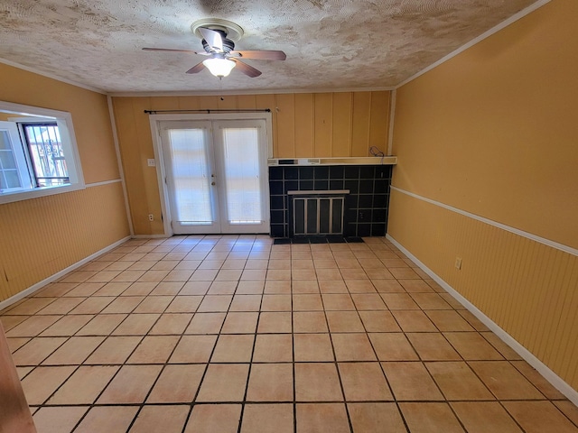 unfurnished living room featuring ceiling fan, french doors, light tile patterned flooring, wood walls, and a textured ceiling