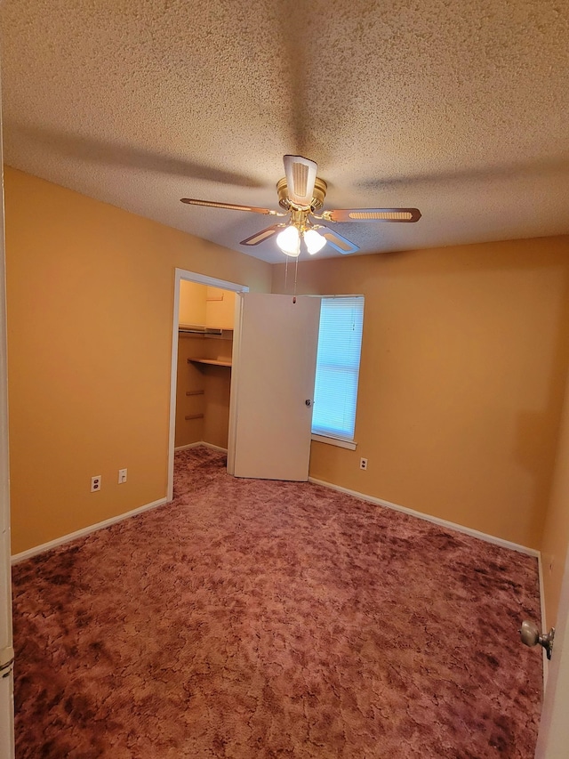 unfurnished bedroom with a walk in closet, carpet, a textured ceiling, and ceiling fan