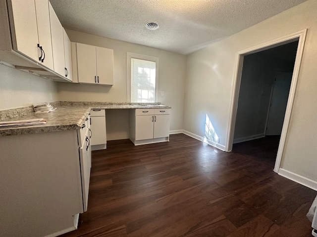 kitchen with built in desk, dark hardwood / wood-style flooring, a textured ceiling, and white cabinetry