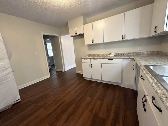 kitchen with dark hardwood / wood-style floors, light stone counters, a textured ceiling, and white cabinetry