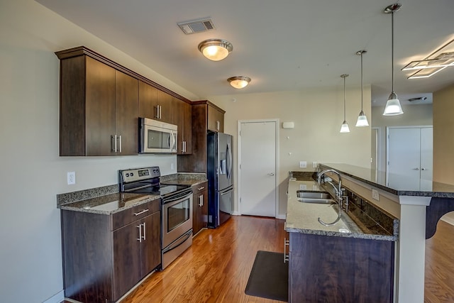 kitchen featuring a breakfast bar area, dark stone counters, sink, light hardwood / wood-style floors, and stainless steel appliances