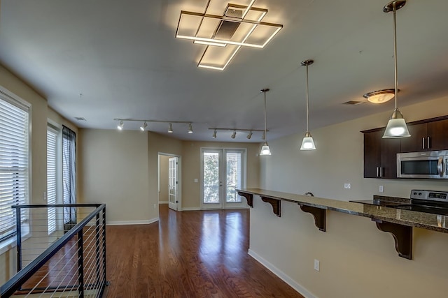 kitchen with appliances with stainless steel finishes, a kitchen bar, dark brown cabinets, dark stone counters, and dark wood-type flooring