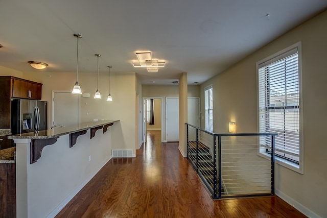 kitchen with dark wood-type flooring, stainless steel fridge, light stone countertops, a breakfast bar, and pendant lighting