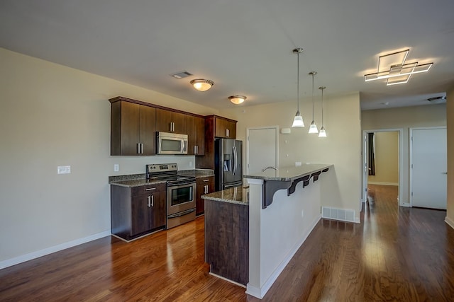 kitchen with appliances with stainless steel finishes, dark brown cabinets, pendant lighting, a breakfast bar, and dark hardwood / wood-style floors