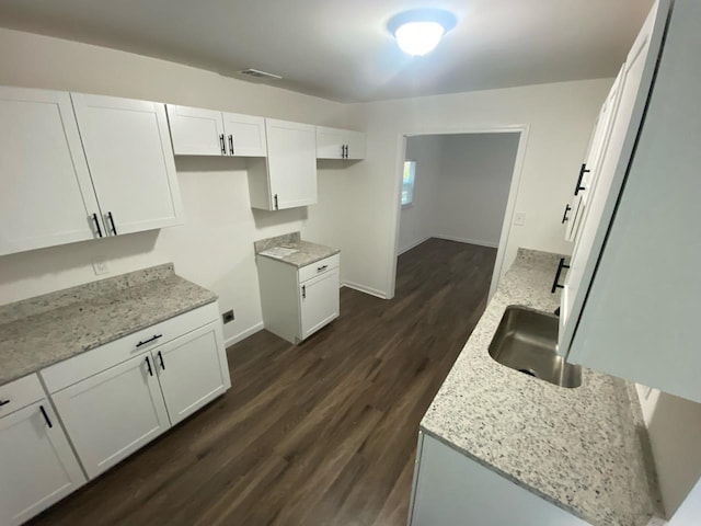 kitchen with light stone counters, white cabinetry, sink, and dark hardwood / wood-style flooring