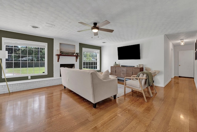 living room featuring a textured ceiling, a brick fireplace, light wood-type flooring, and ceiling fan