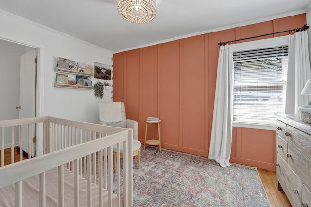 bedroom with a nursery area, crown molding, and light hardwood / wood-style floors