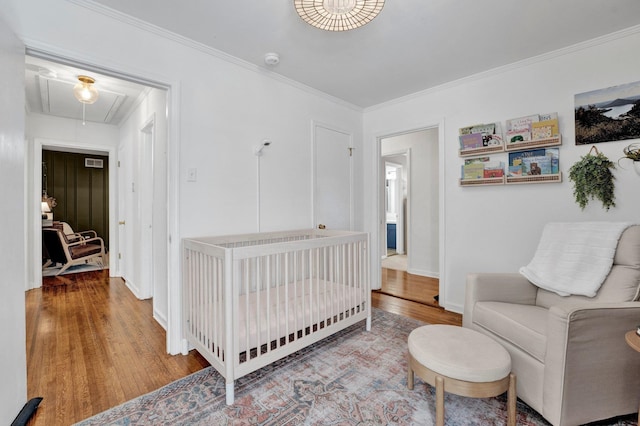 bedroom featuring a crib, crown molding, and hardwood / wood-style floors